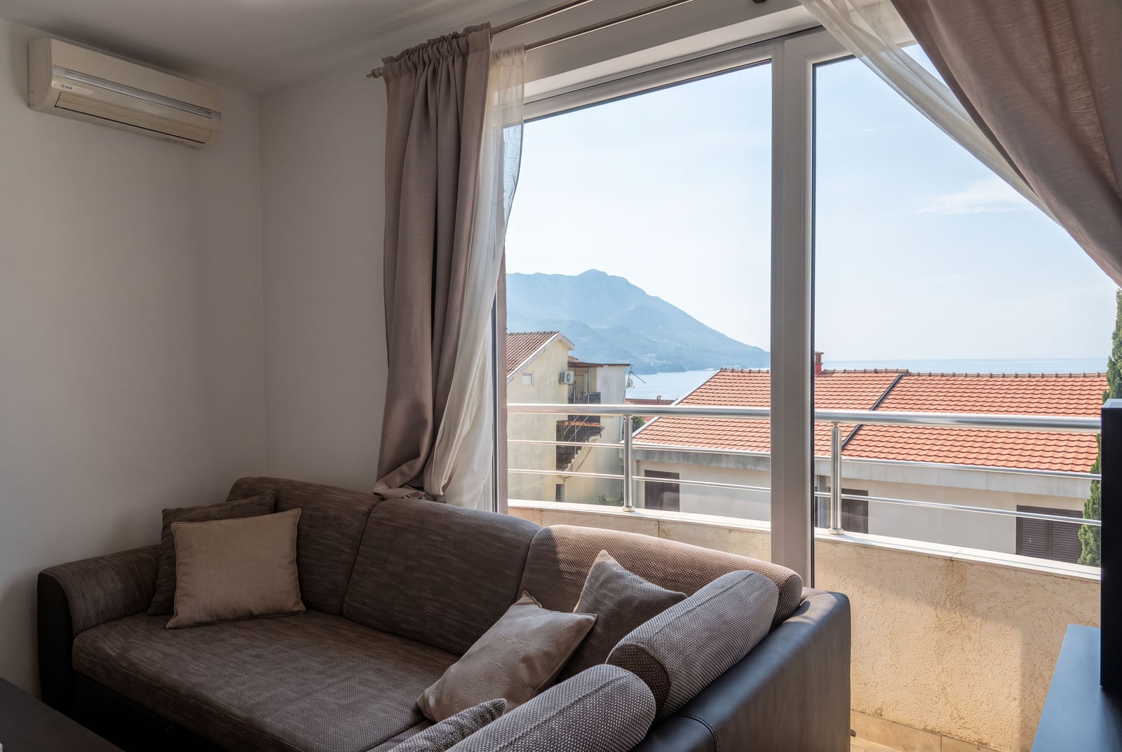 Dnevna soba sa udobnom sofom i panoramskim prozorom sa pogledom na more i planine u Bečićima, Crna Gora