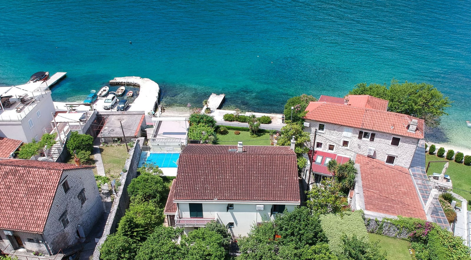 Luftaufnahme einer Villa in Dobrota, Montenegro: Steinhäuser, Pool, grüner Garten und direkter Zugang zum Meer mit Steg.
