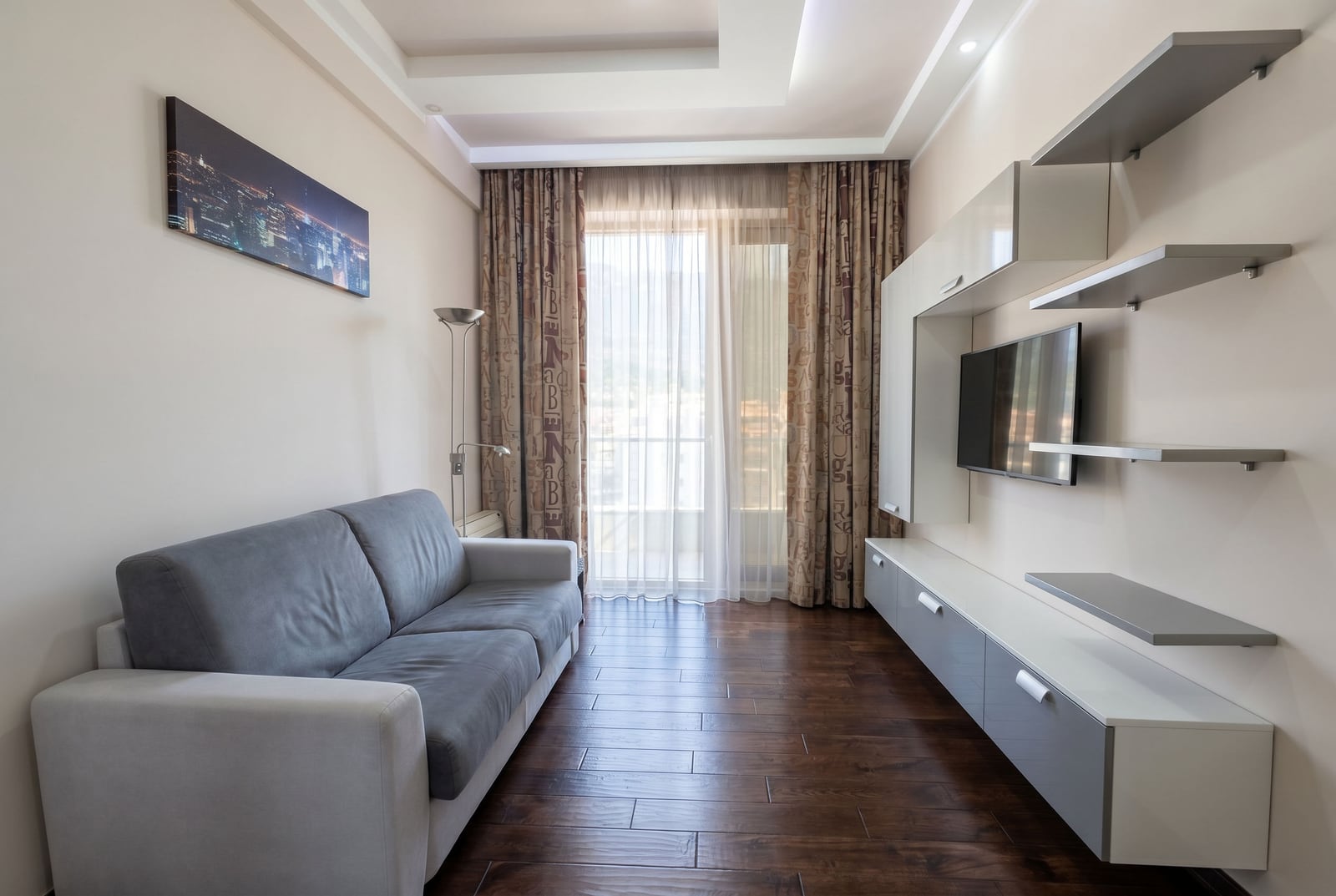 Modern living room with a grey sofa and TV area in a Budva apartment, Montenegro: stylish interior with balcony access.