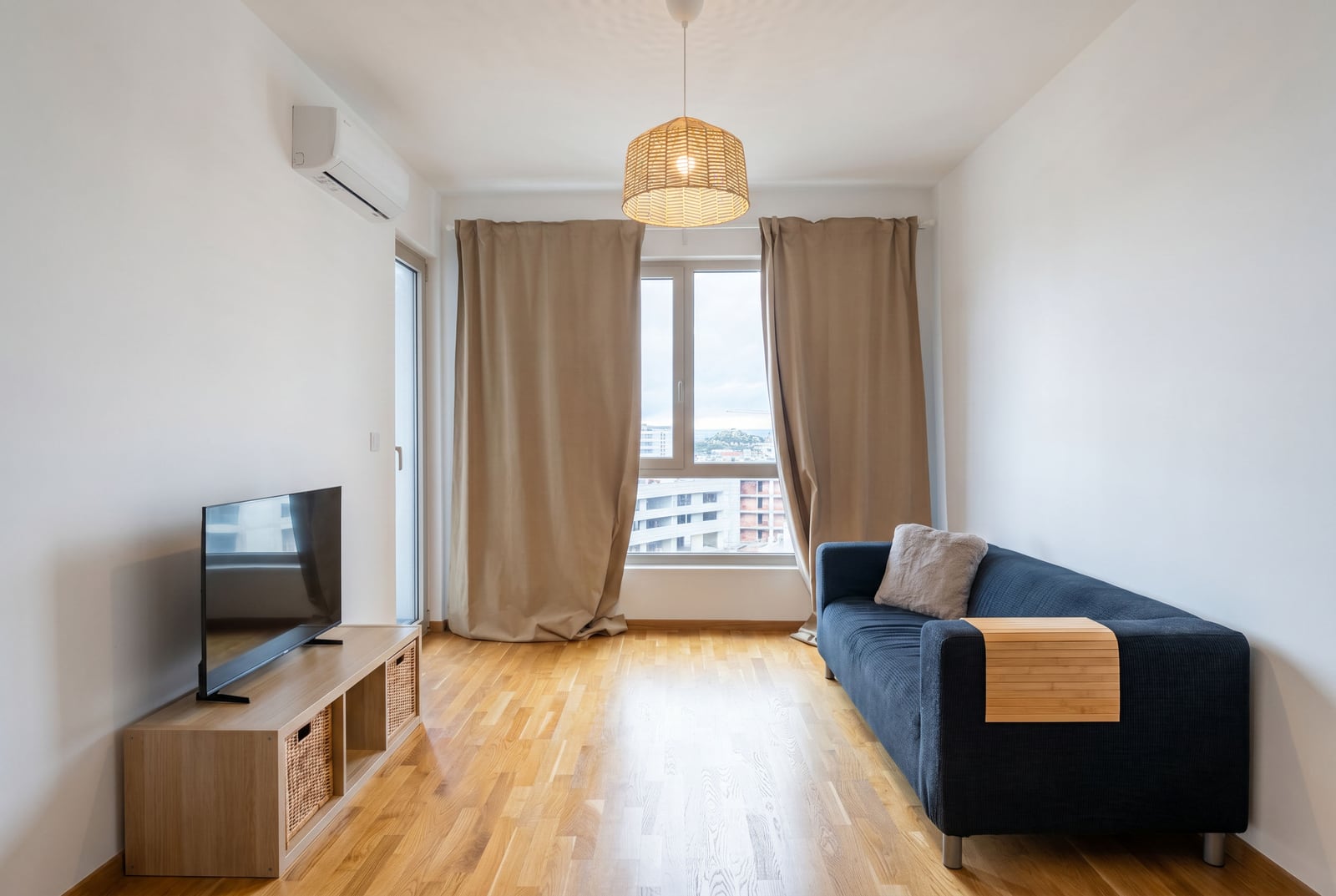 Bright living room with a blue sofa and parquet flooring in an apartment in Becici, Montenegro, with a view of the city from the window.