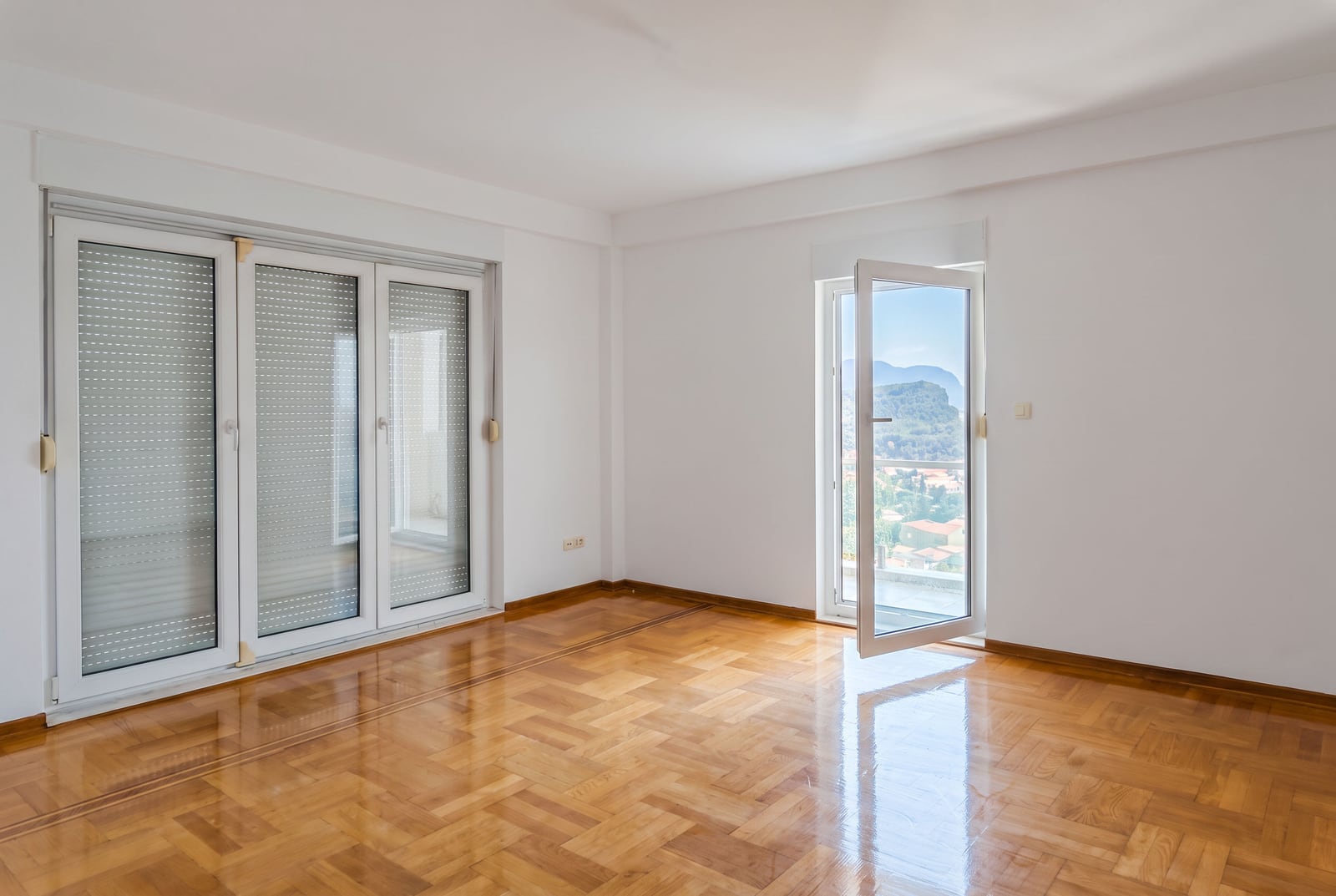Bright empty living room with parquet flooring, panoramic windows, and mountain views in an apartment in Petrovac, Montenegro.