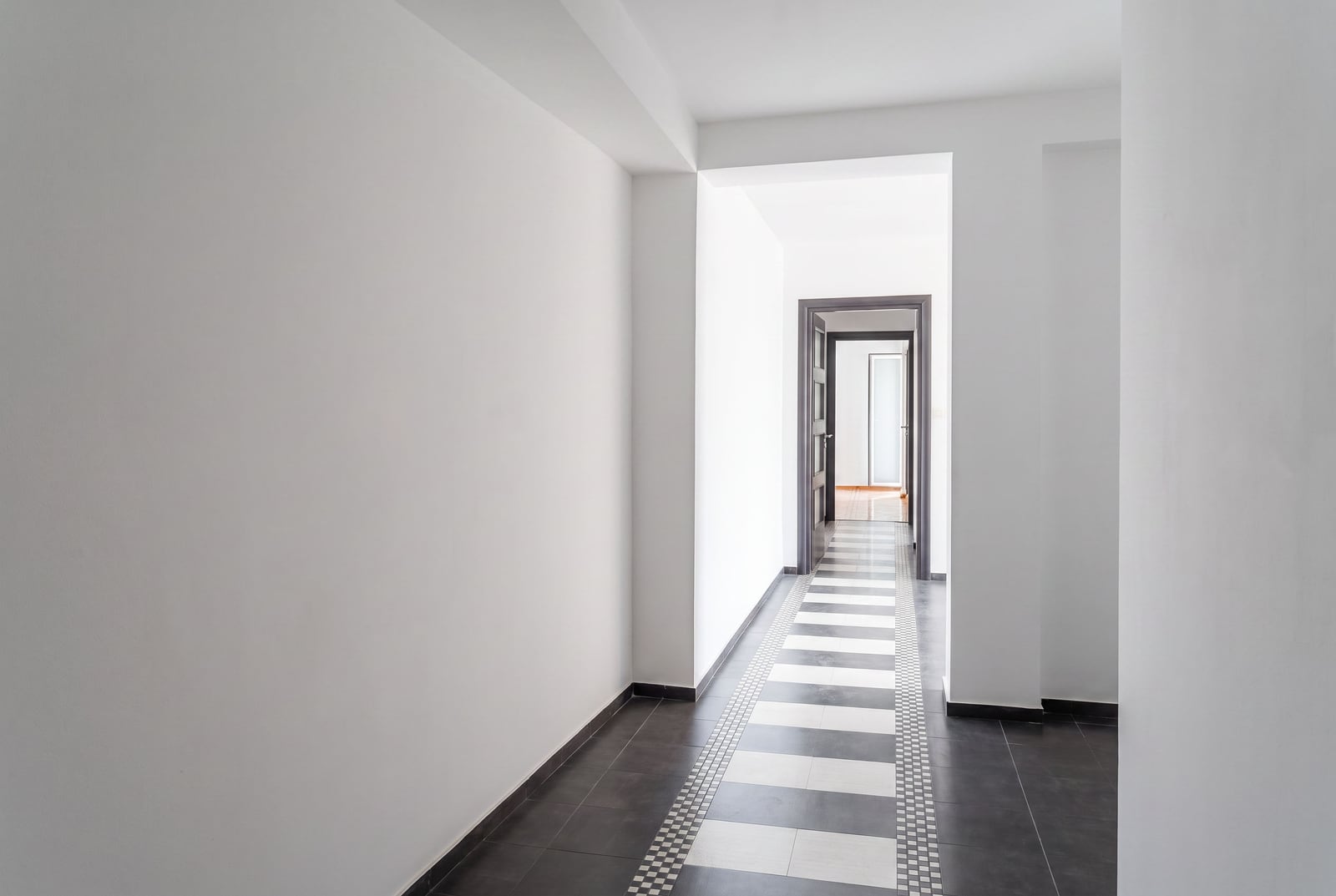 Bright long hallway with white walls and black-and-white tile flooring in an apartment in Petrovac, Montenegro