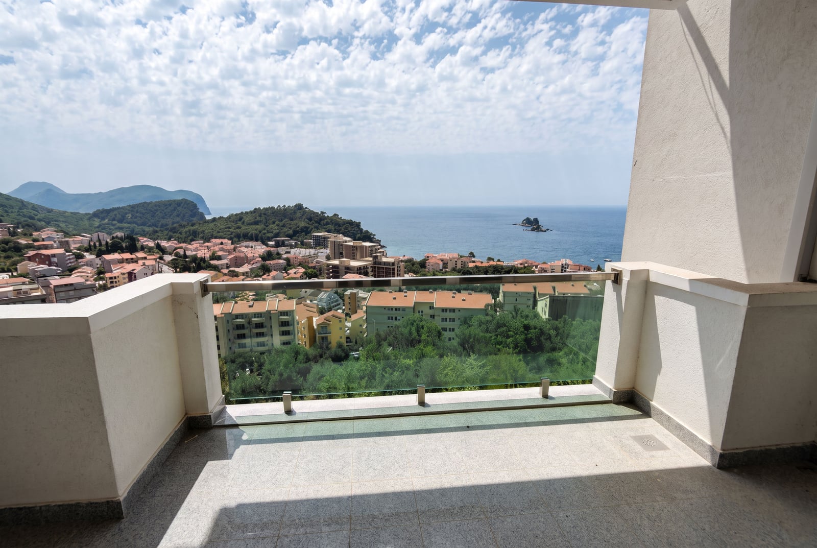 Panoramic view of the sea and the town of Petrovac, Montenegro, from a spacious balcony with glass railing.