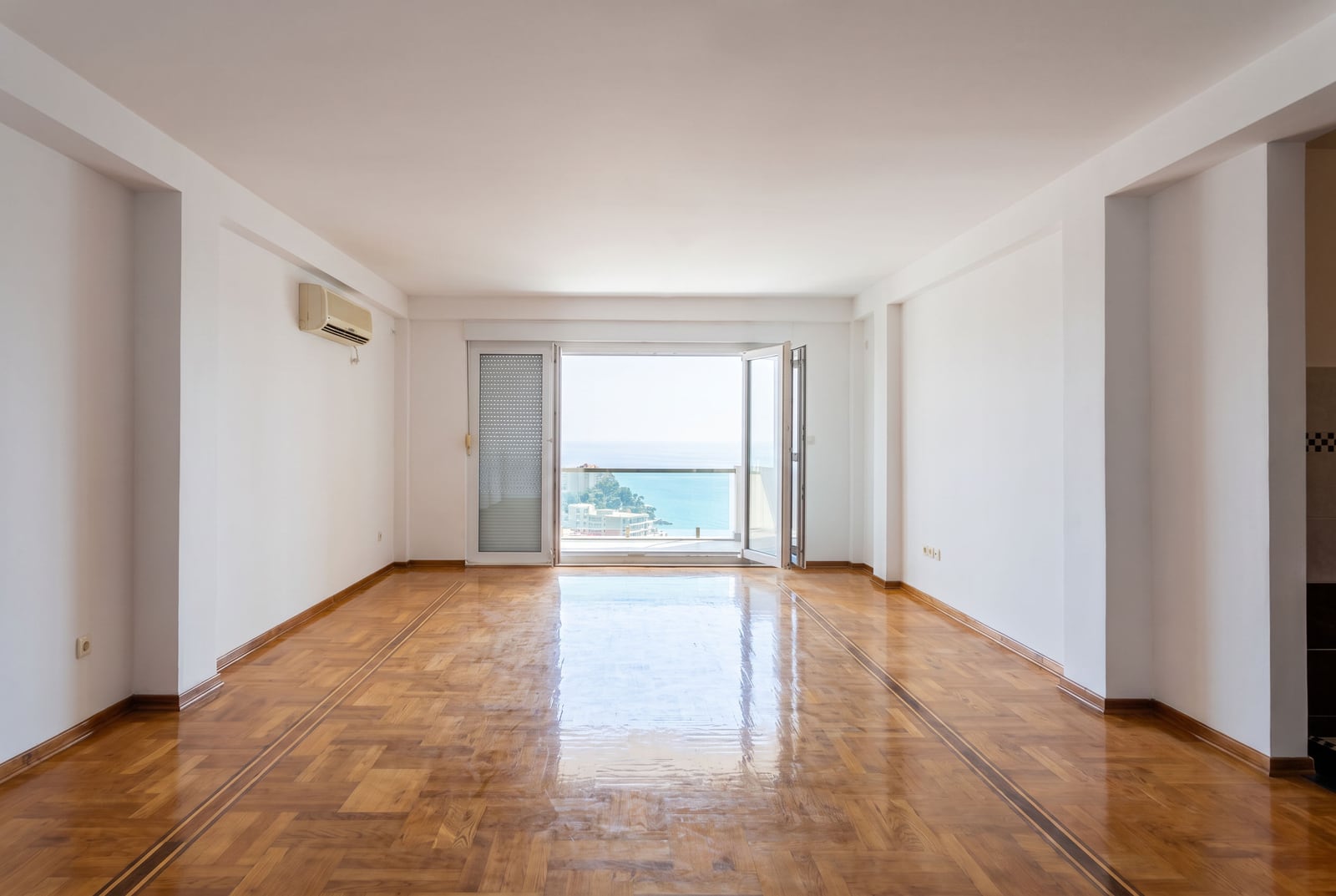 Spacious bright living room with parquet flooring, white walls, and panoramic access to a balcony with sea views in Petrovac, Montenegro.