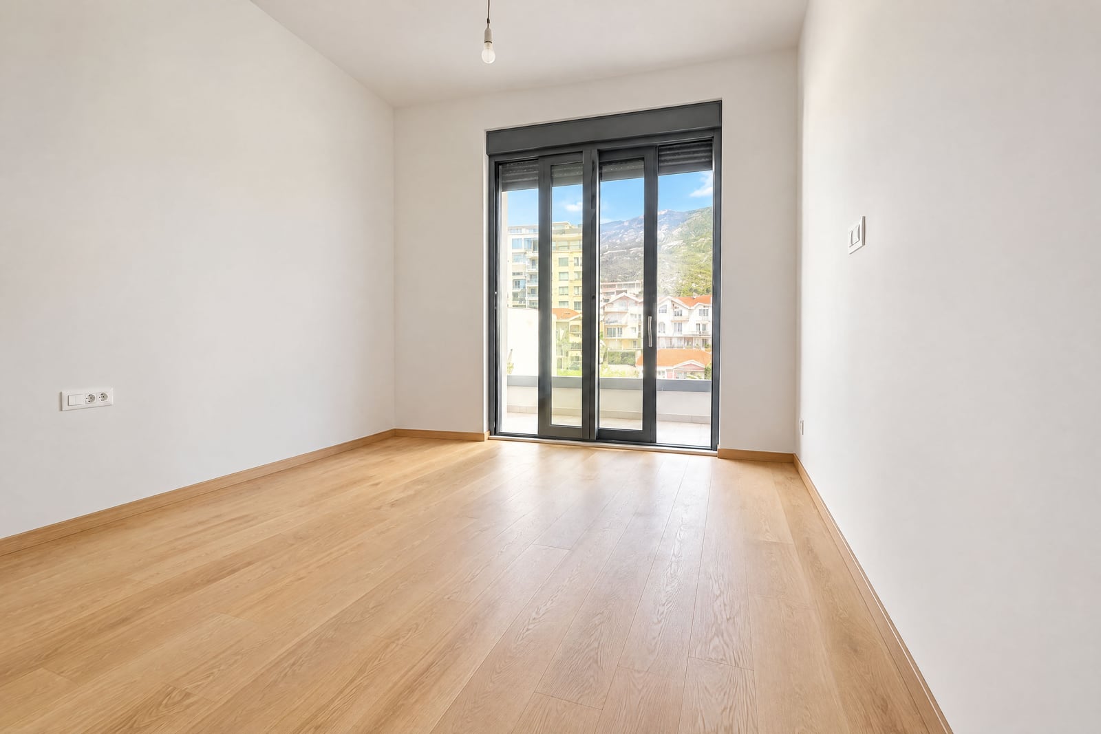 Bright empty bedroom with parquet flooring and a panoramic mountain-view window in an apartment, Montenegro