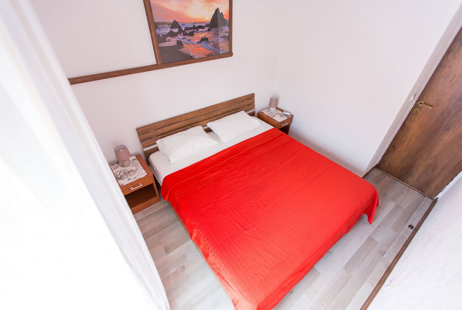 Cozy bedroom with a wooden bed and red bedspread in an apartment in Budva, Montenegro.