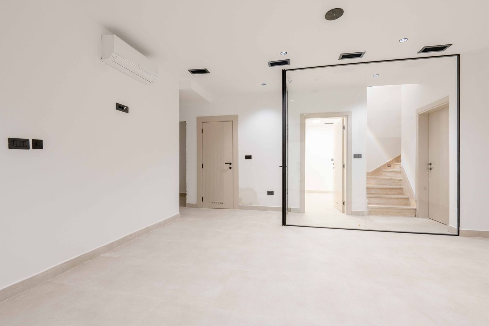 Salon moderne avec finition blanche, cloison vitrée et escalier dans une villa à Kamenovo, Monténégro.