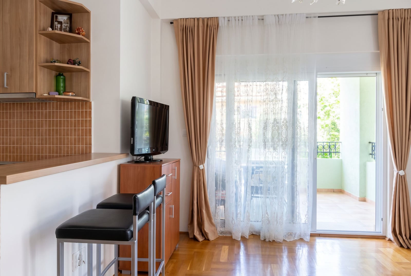Karadağ, Budva'da satılık dairede bar tezgahı ve balkon çıkışı olan oturma odası. Parke zemin, TV ve aydınlık iç mekan.