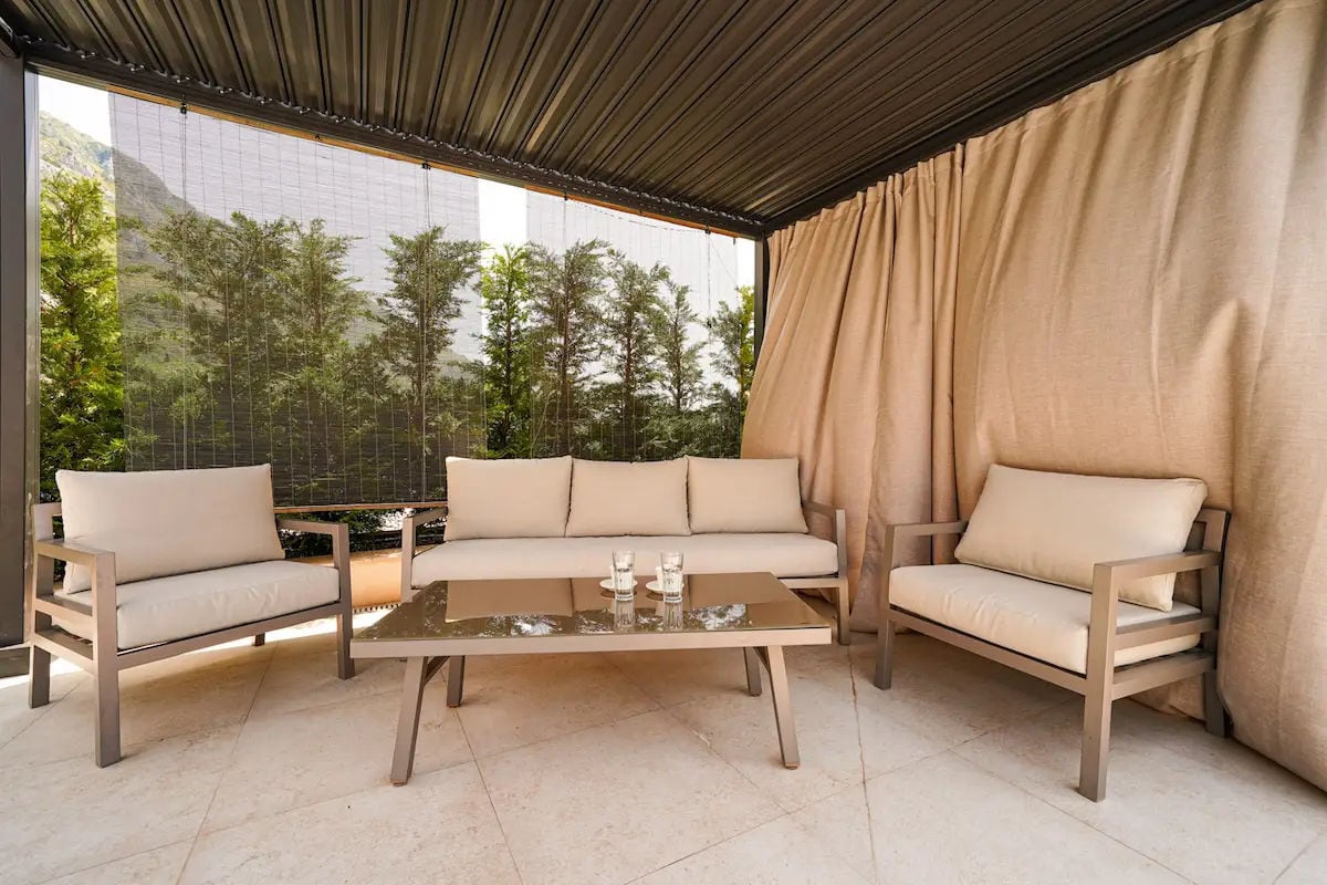 Terrasse confortable avec mobilier moelleux dans une villa à Reževići, Monténégro : vue sur les montagnes, auvent et intérieur élégant.