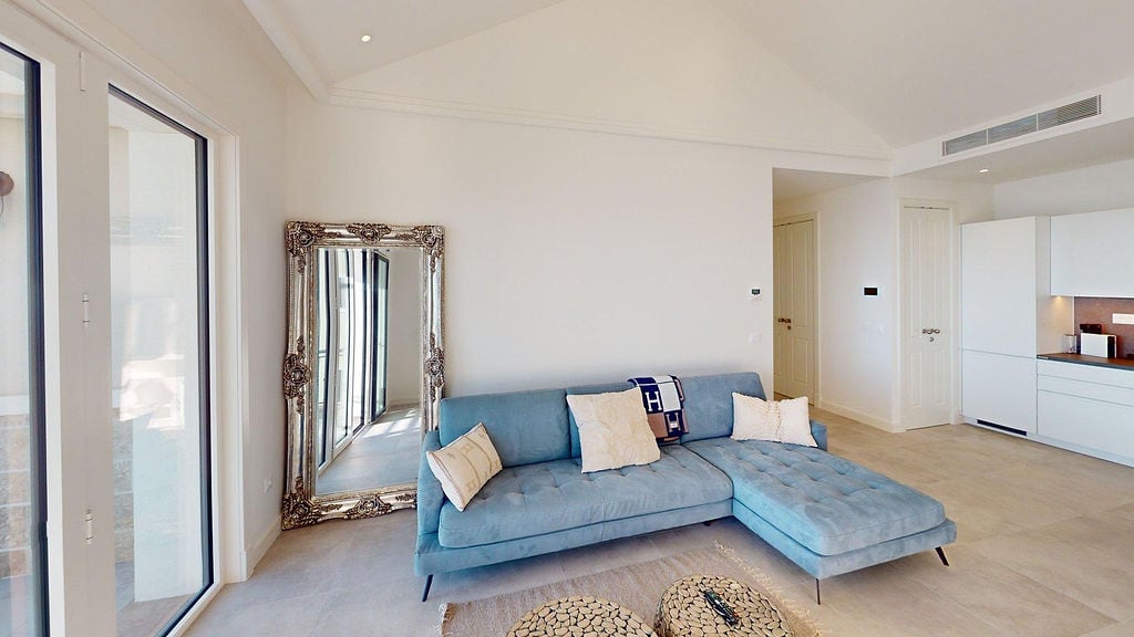 Modernes Wohnzimmer mit blauem Sofa und Spiegel in einer Wohnung in Luštica, Montenegro. Helle Inneneinrichtung mit Küche.