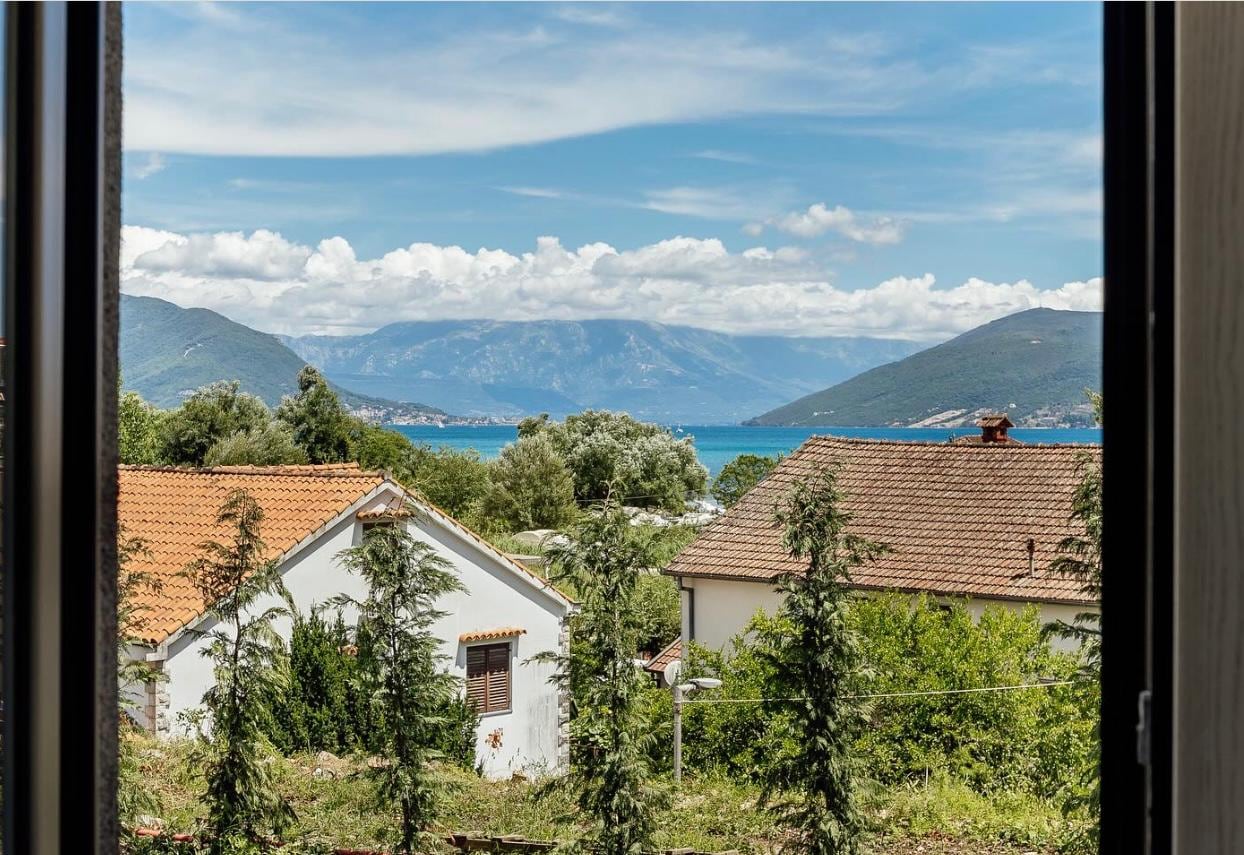 Blick aus dem Fenster eines Apartments in Igalo, Montenegro: malerische Aussicht auf das Meer, die Berge und die Ziegeldächer der Häuser.