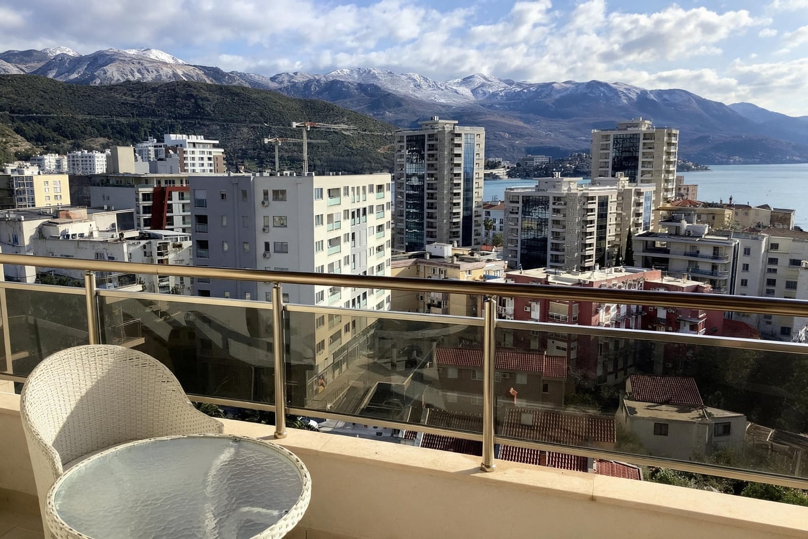 Balcony with wicker furniture and panoramic views of the city, sea, and mountains in Budva, Montenegro.