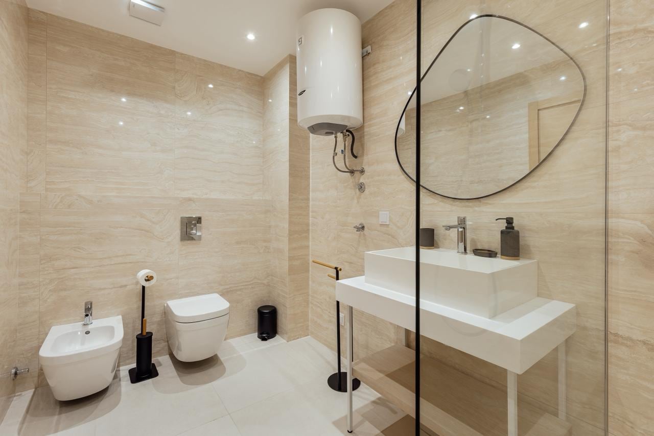 Modernes Badezimmer in einer Wohnung in Igalo, Montenegro: beige Fliesen, Duschkabine und ein stilvoller Spiegel.