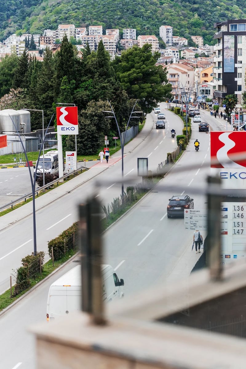 Pogled sa balkona stana u Budvi, Crna Gora: gradska ulica, EKO benzinska pumpa i planinski pejzaž u pozadini.
