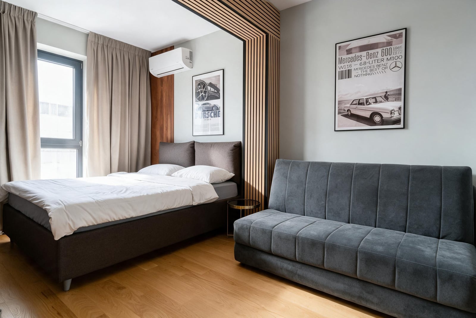 Modern bedroom with a double bed, gray sofa, and wooden slats in an apartment in Budva, Montenegro.