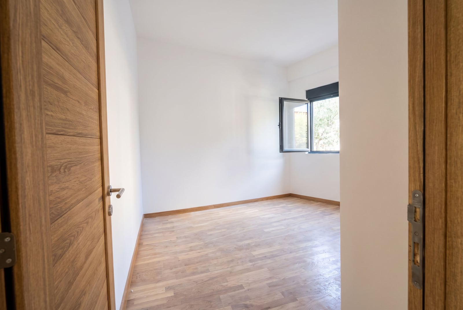 Bright empty bedroom with parquet flooring and wooden doors in an apartment in the city of Bar, Montenegro.