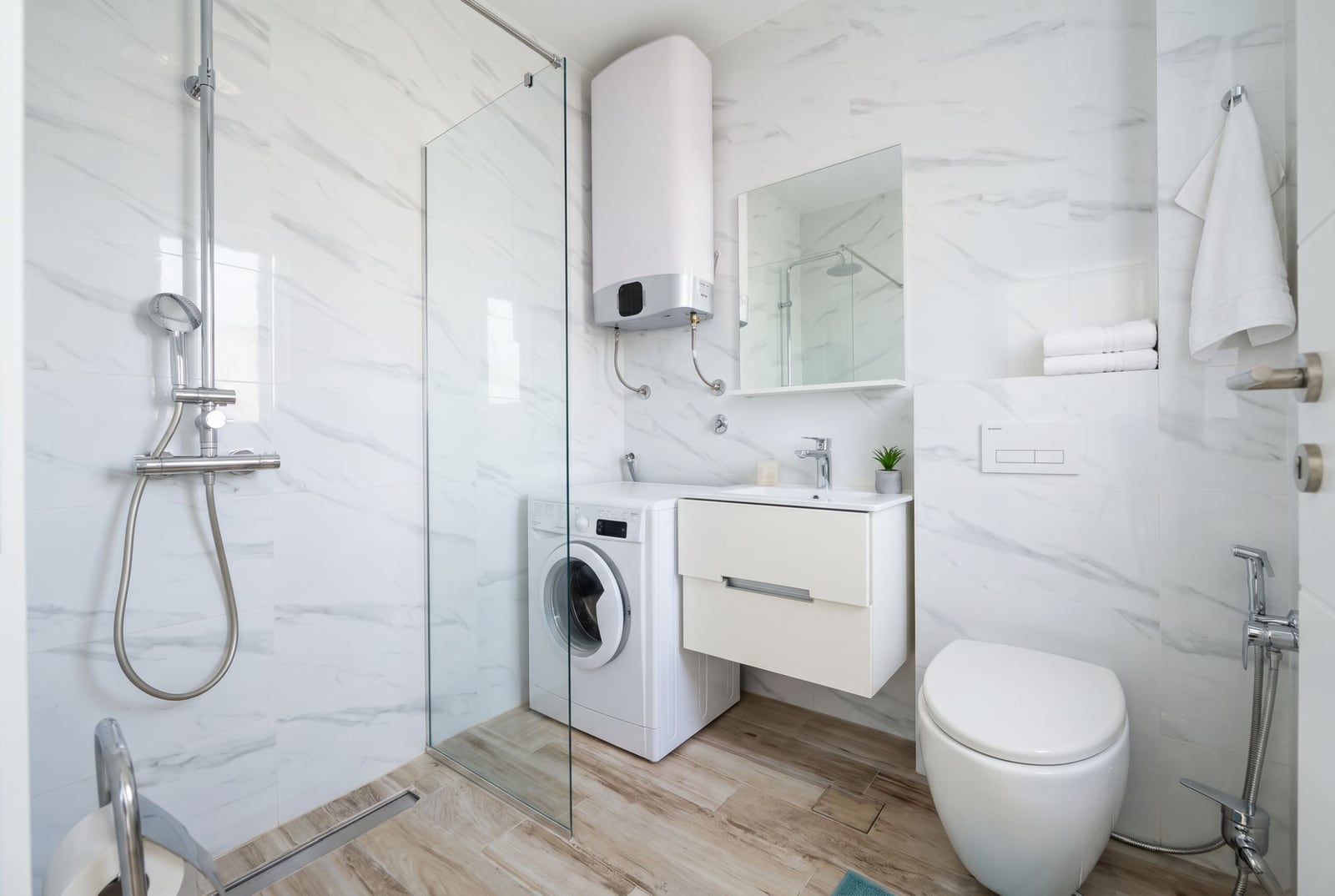 Modernes Badezimmer in einer Wohnung in Bečići, Montenegro: Duschkabine, Waschmaschine und helle Ausstattung.