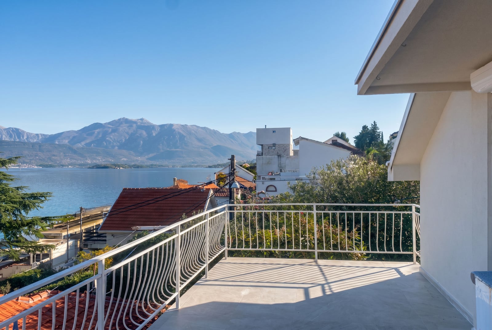 Terrasse spacieuse d'une maison à Krašići, Monténégro, avec vue panoramique sur la mer et les montagnes, finitions lumineuses et garde-corps blancs.