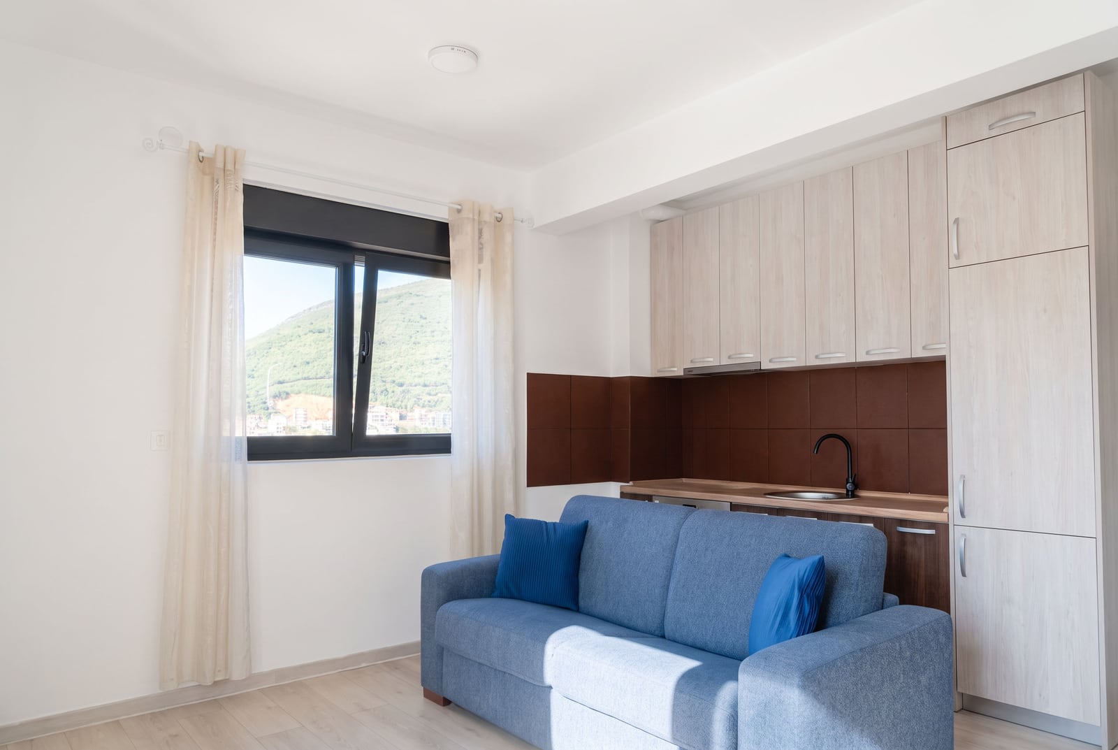 Modern kitchen-living room with a blue sofa and mountain view in an apartment in Budva, Montenegro