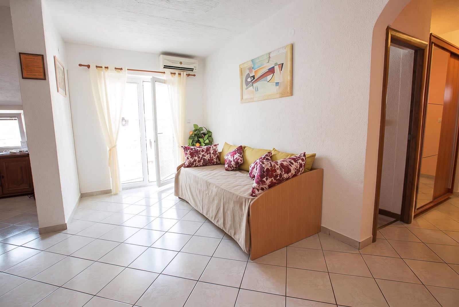 Bright living room with white finishes, tile flooring, a sofa, and access to a balcony in an apartment in Budva, Montenegro.