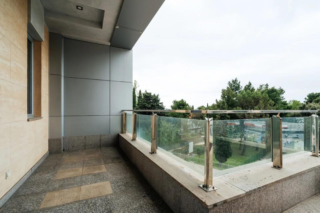 Prostran balkon sa panoramskom ogradom i pogledom na zelenilo u modernom stanu, Budva, Crna Gora.