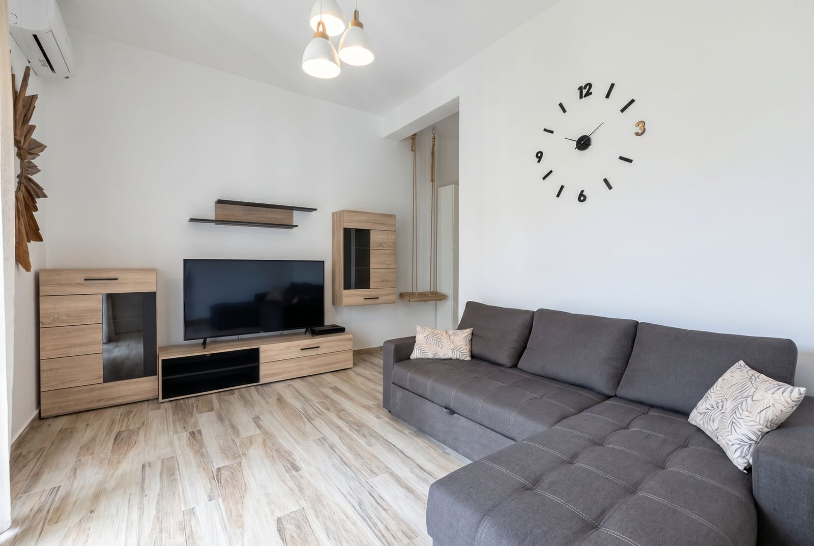 Modernes Wohnzimmer in einer Wohnung in Bečići, Montenegro: graues Ecksofa, TV-Bereich, Wanduhr und Schaukel.