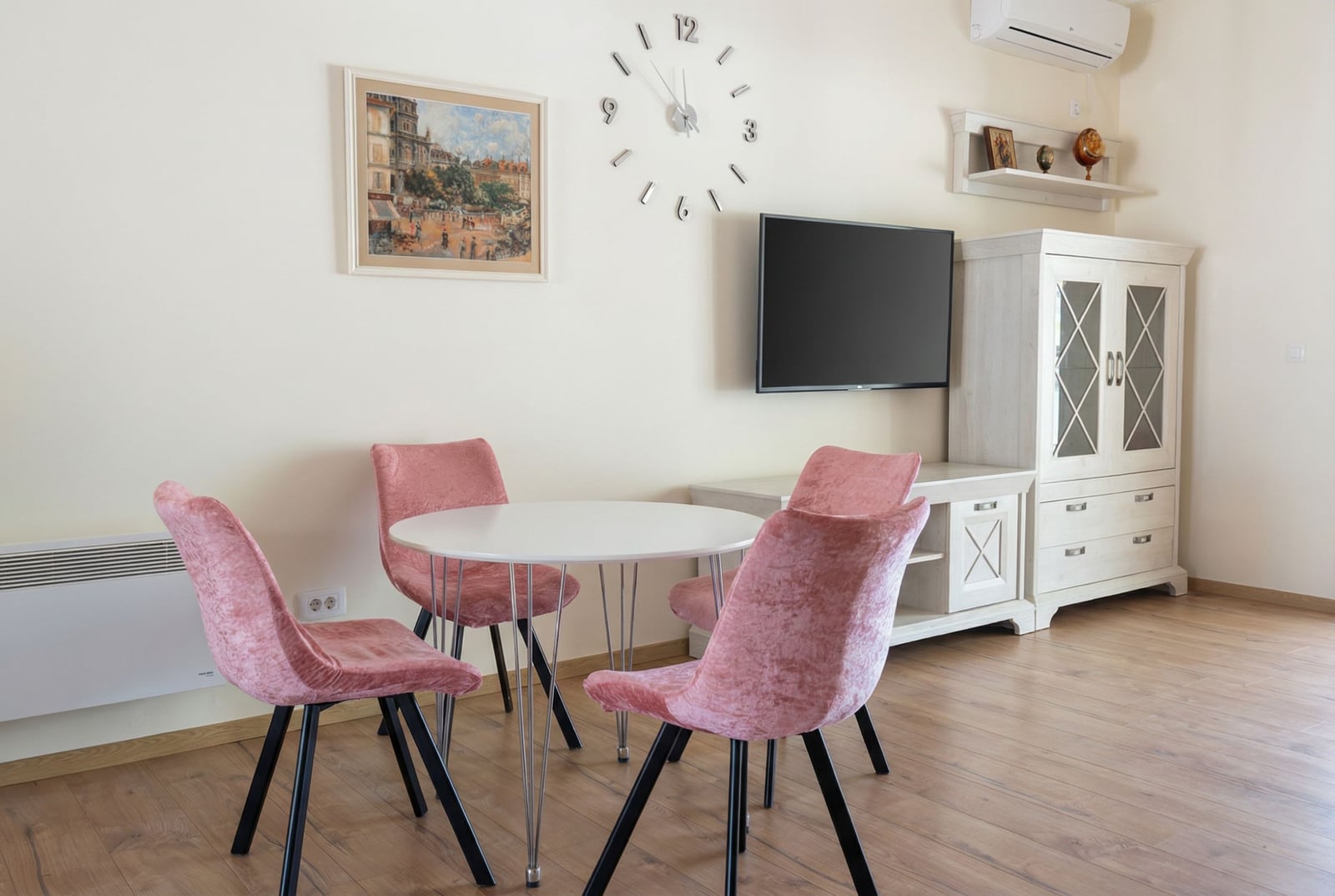 Dnevna soba u stanu u Pržnu, Crna Gora: trpezarijski deo sa ružičastim baršunastim stolicama, TV-om i svetlim nameštajem.