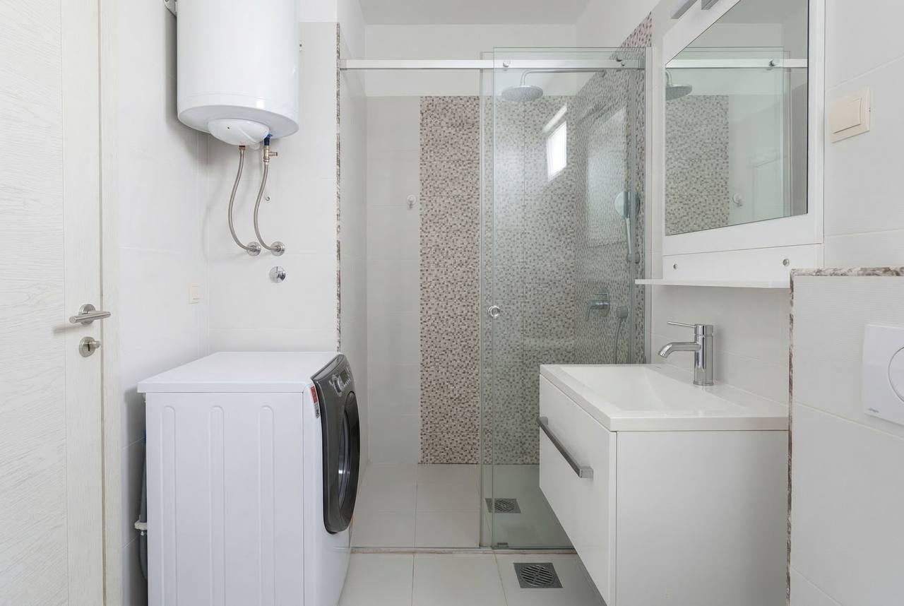 Modern bathroom in an apartment in Bečići, Montenegro: shower cabin, washing machine, and white furniture.