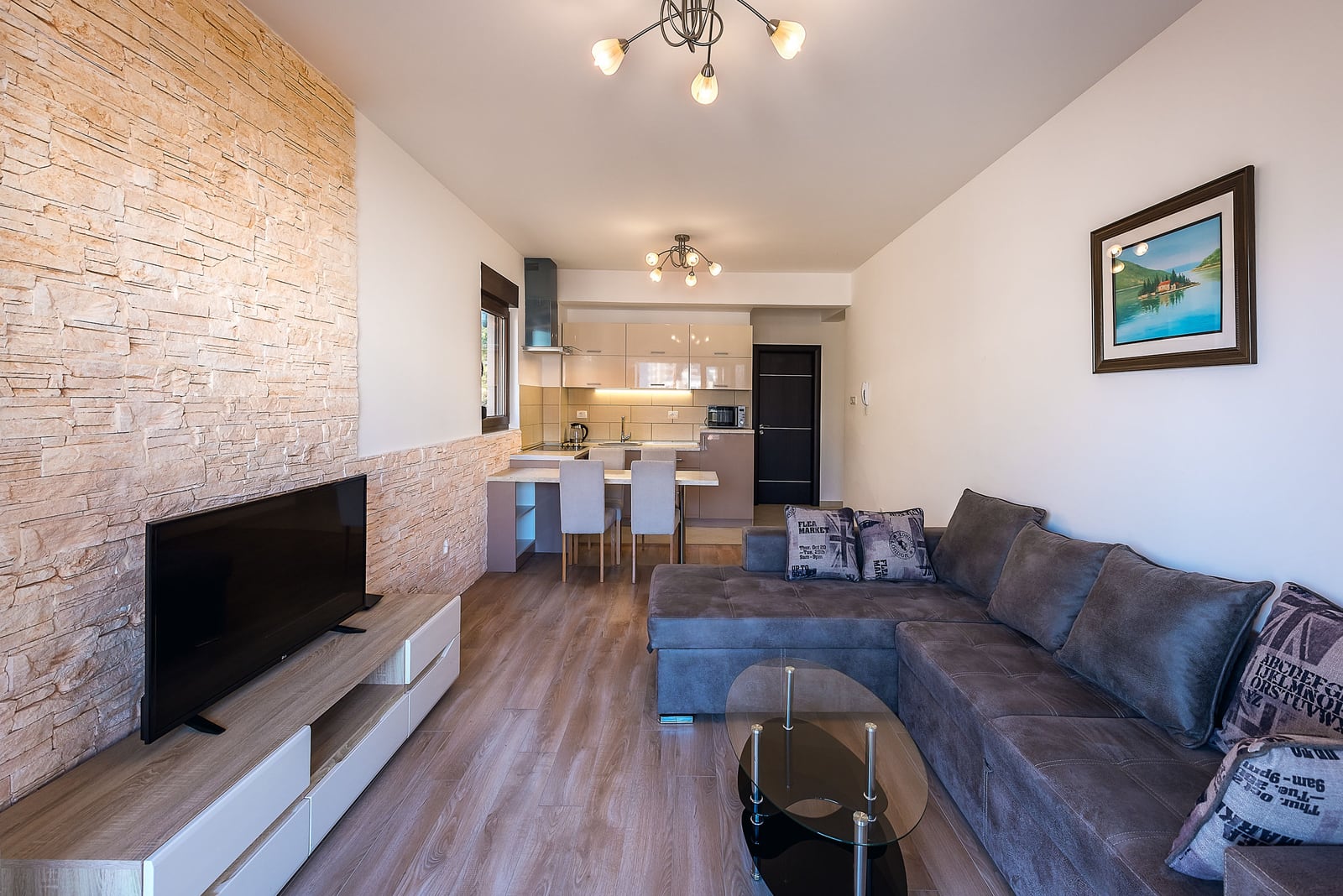 Living room with kitchen in an apartment in Budva, Montenegro: corner sofa, stone finish, and modern furniture.