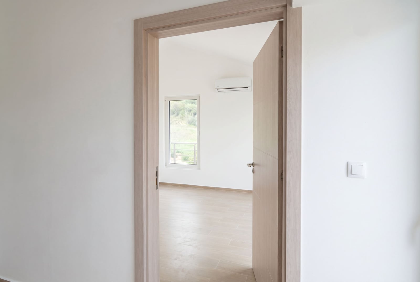 Светлая спальня в квартире, Дженовичи, Черногория: межкомнатная дверь, белые стены, кондиционер и вид из окна.