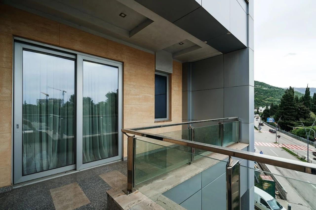 Moderan balkon sa panoramskim ostakljenjem u stanu, Budva, Crna Gora: pogled na grad i planine, završna obrada fasade.