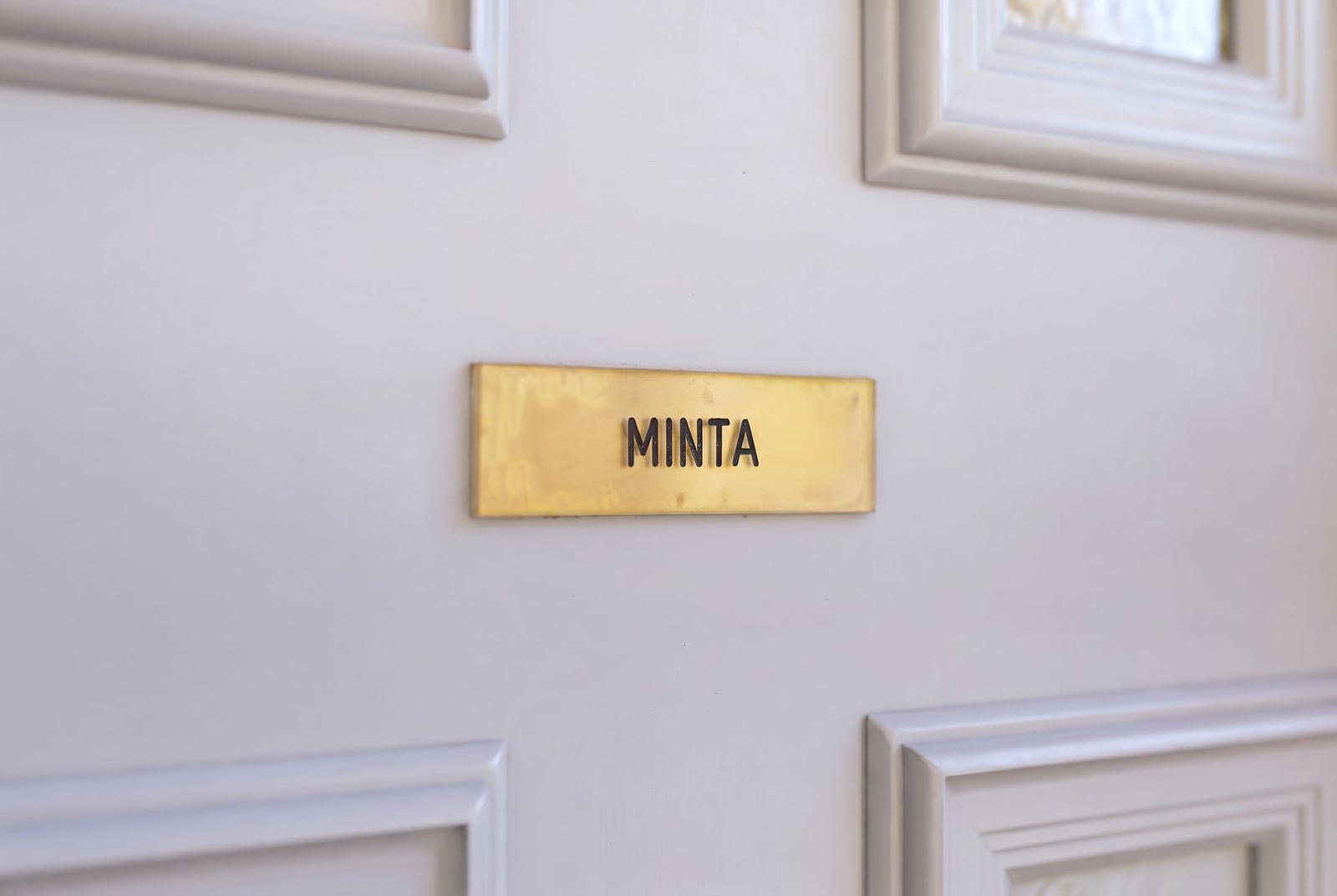 Золотая табличка с надписью Minta на белой филенчатой двери апартаментов в городе Рисан, Черногория.