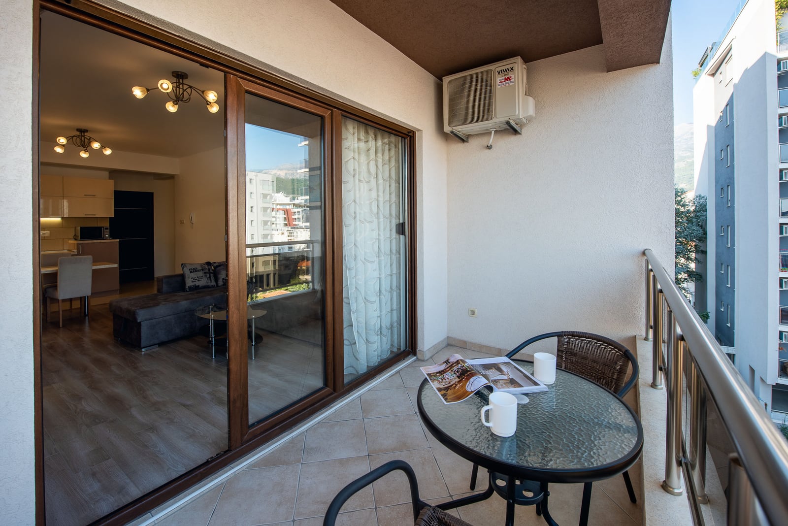 Balcony with furniture and city view in an apartment in Budva, Montenegro: panoramic windows, living room, and modern kitchen.