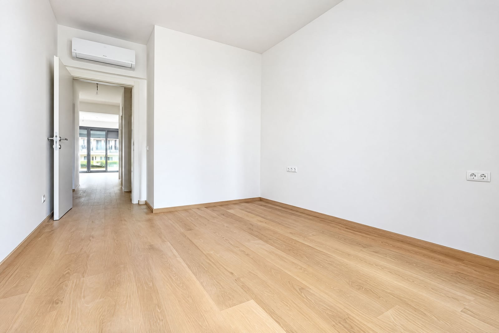 Bright empty bedroom with white walls, parquet flooring, and air conditioning in an apartment in Becici, Montenegro