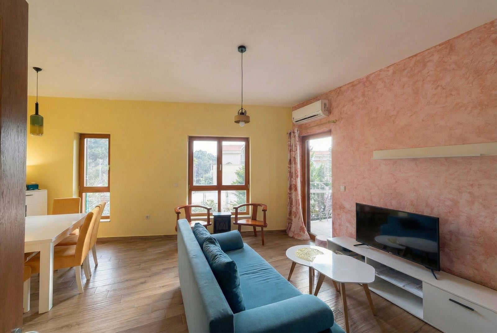 Living room with a blue sofa and dining area in an apartment in Petrovac, Montenegro: modern interior with access to the balcony.