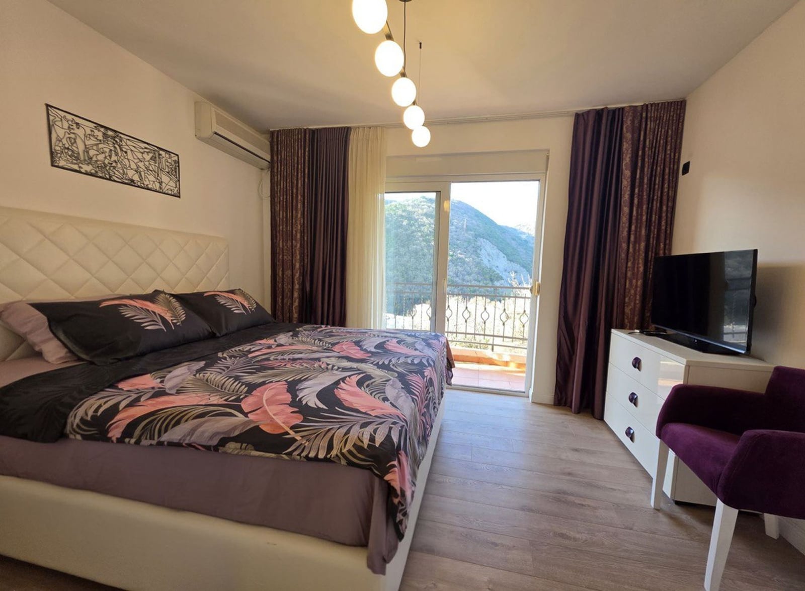 Spavaća soba u stanu u Bečićima, Crna Gora: bračni krevet, TV, komoda i balkon s pogledom na planine.