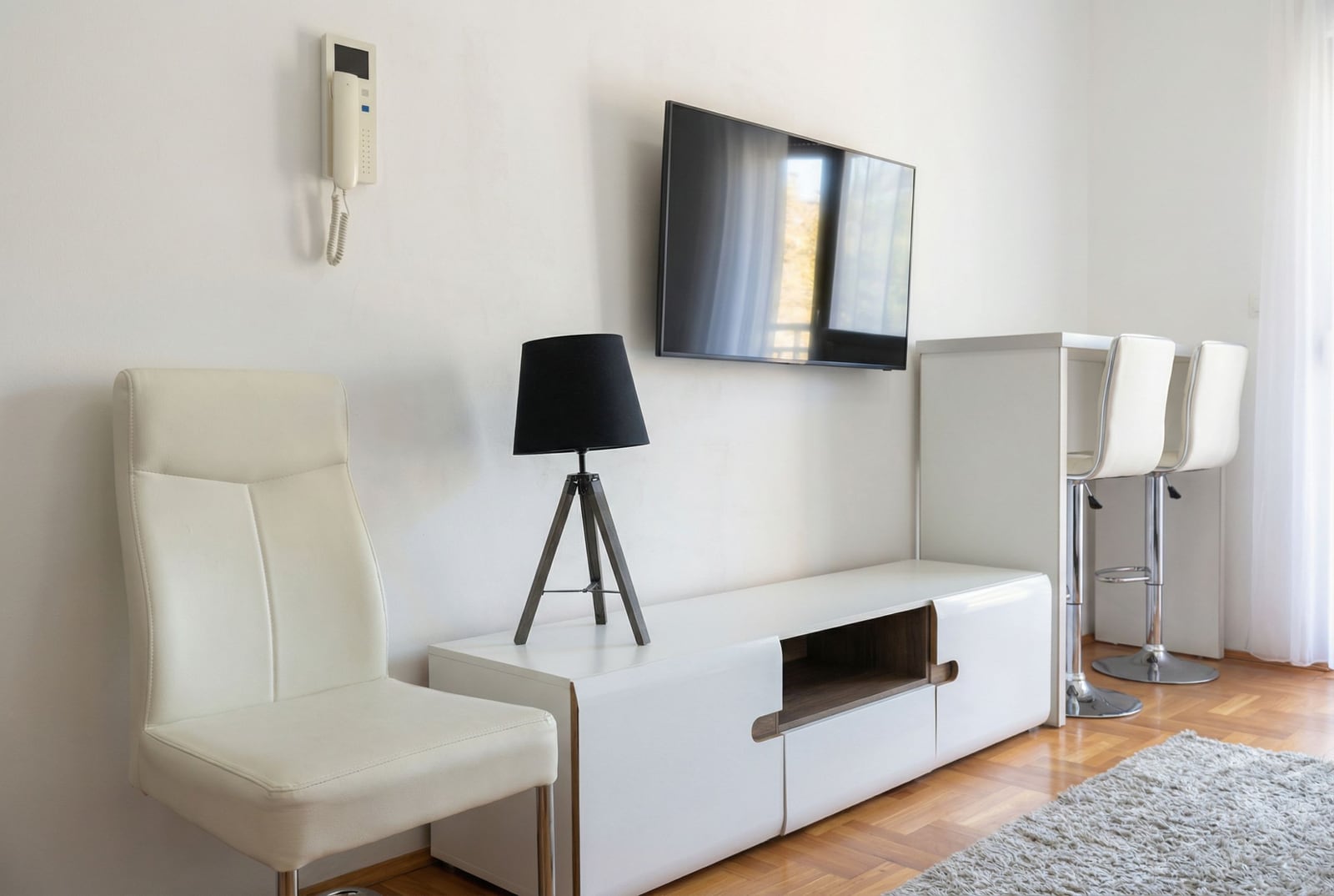 Savremena dnevna soba u stanu u Budvi, Crna Gora: beli nameštaj, TV, barski pult i parket.