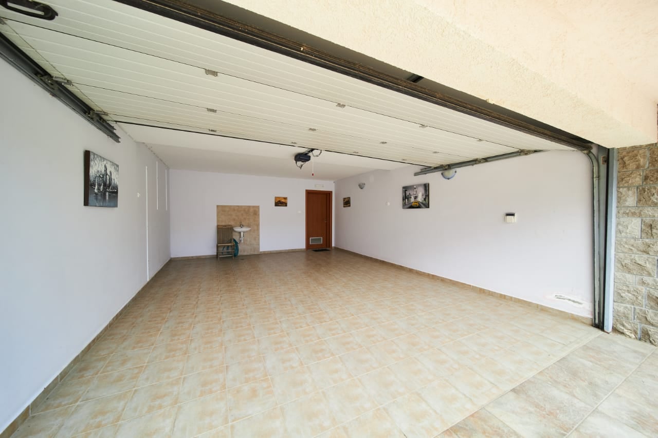 Garage spacieux avec porte automatique et sol carrelé dans une villa à Bečići, Monténégro.