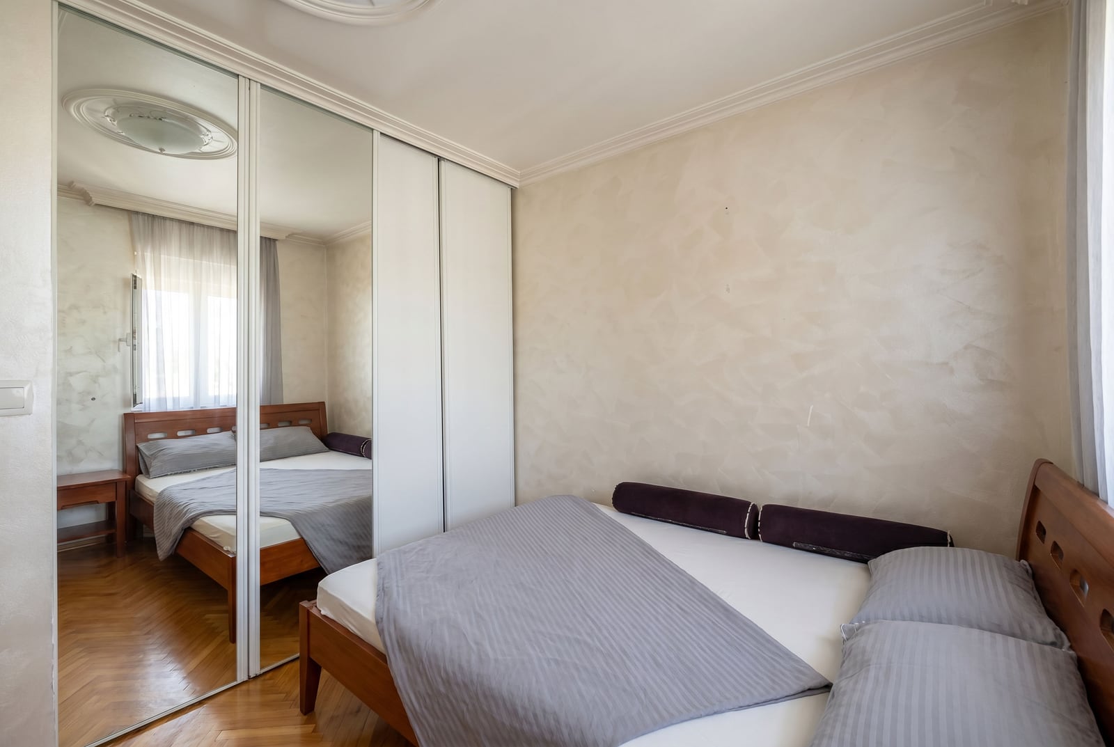Bedroom in a Budva apartment, Montenegro: featuring a double bed, a mirrored sliding-door wardrobe, and parquet flooring.