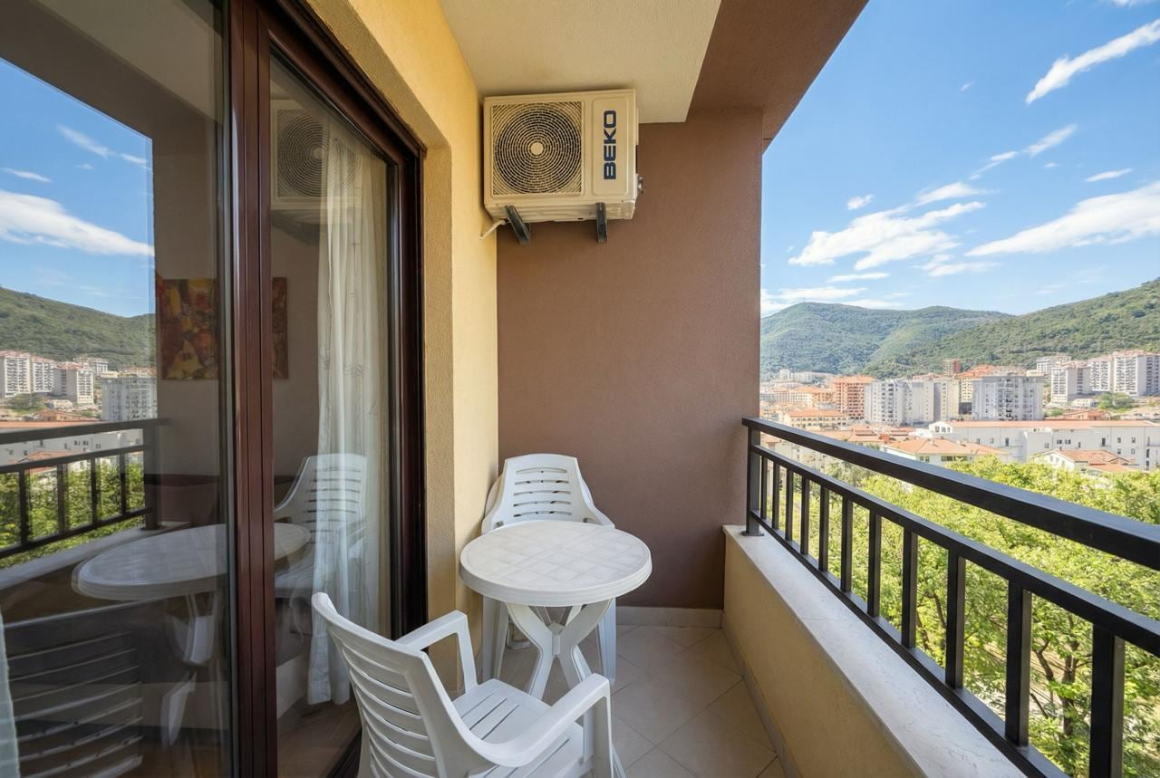 Apartment balcony in Budva, Montenegro: plastic furniture, mountain and city views, panoramic glazing, air conditioning.