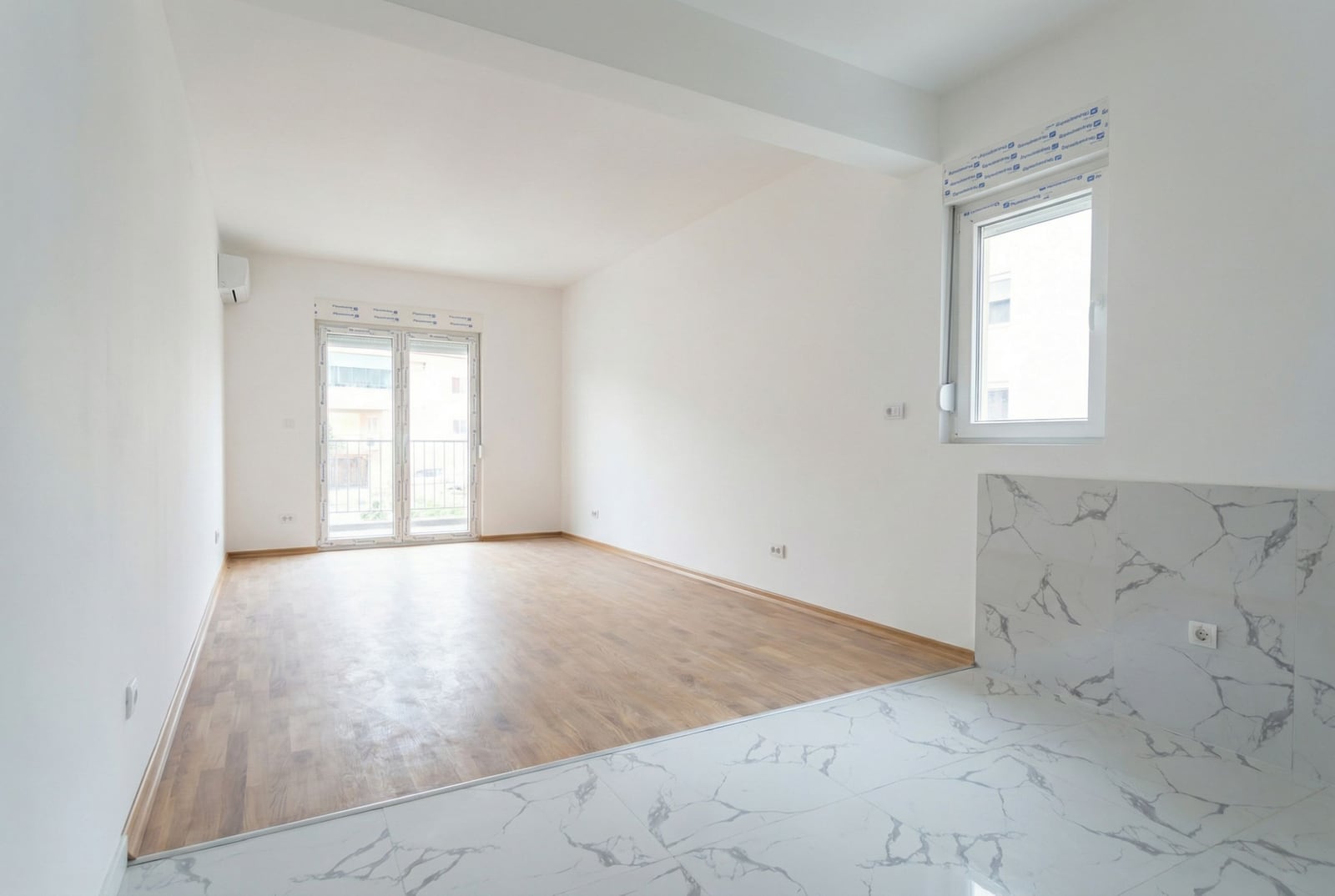 Svetao dnevni boravak u novom stanu u Budvi, Crna Gora: kombinovani pod, beli zidovi i izlaz na balkon.