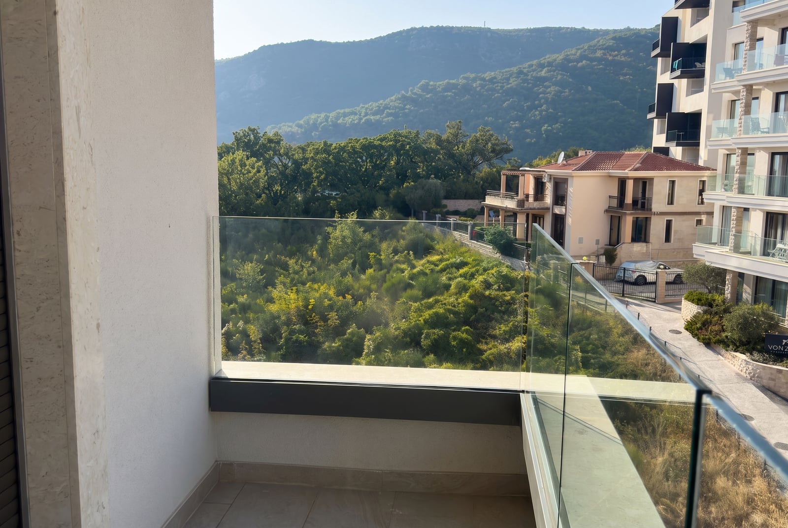 Vue depuis le balcon d'un appartement à Bečići, Monténégro : panorama sur les montagnes verdoyantes, la forêt et les maisons modernes voisines.