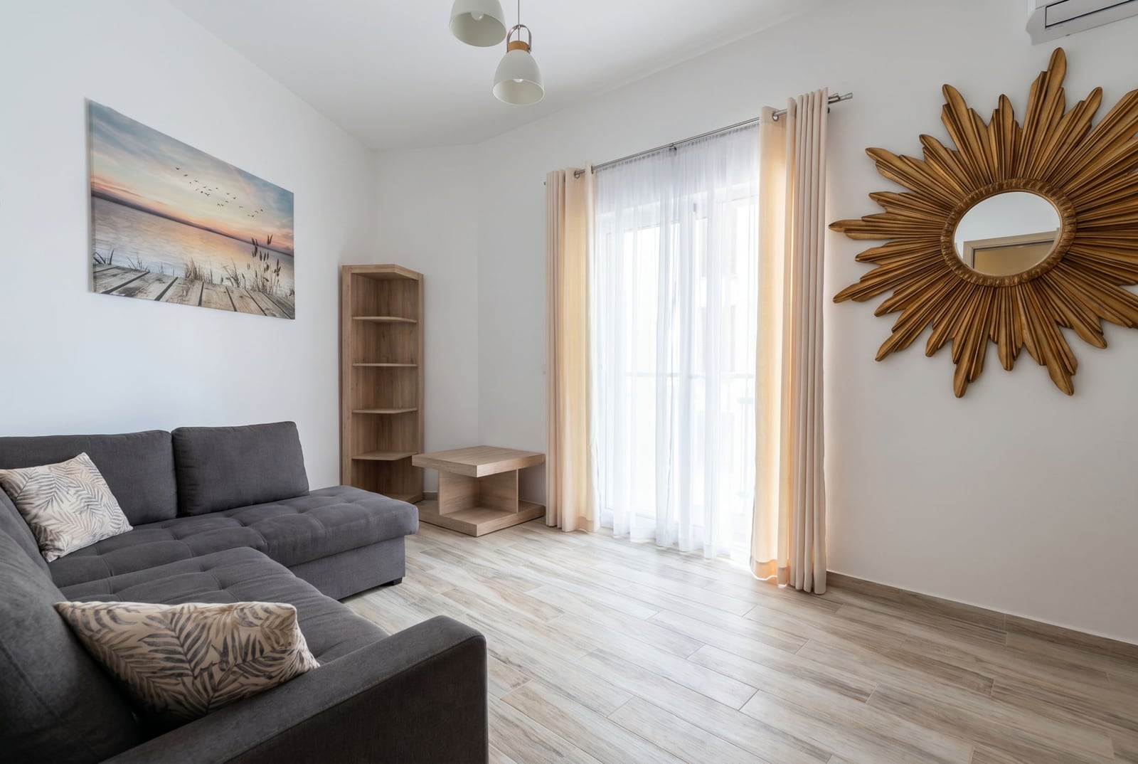 Helles Wohnzimmer in einer Wohnung in Bečići, Montenegro: graues Sofa, Holzregal, Dekor und Zugang zum Balkon.