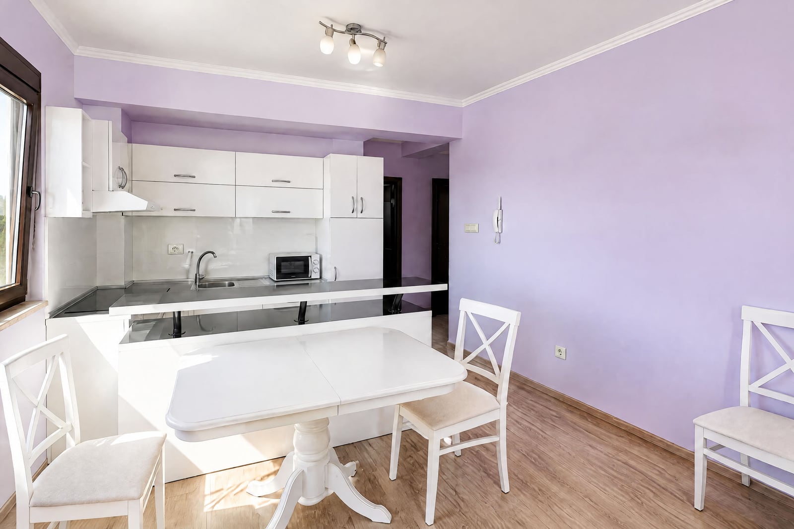Modern kitchen in an apartment in Budva, Montenegro: white furniture, bar counter, dining table, and lilac walls.