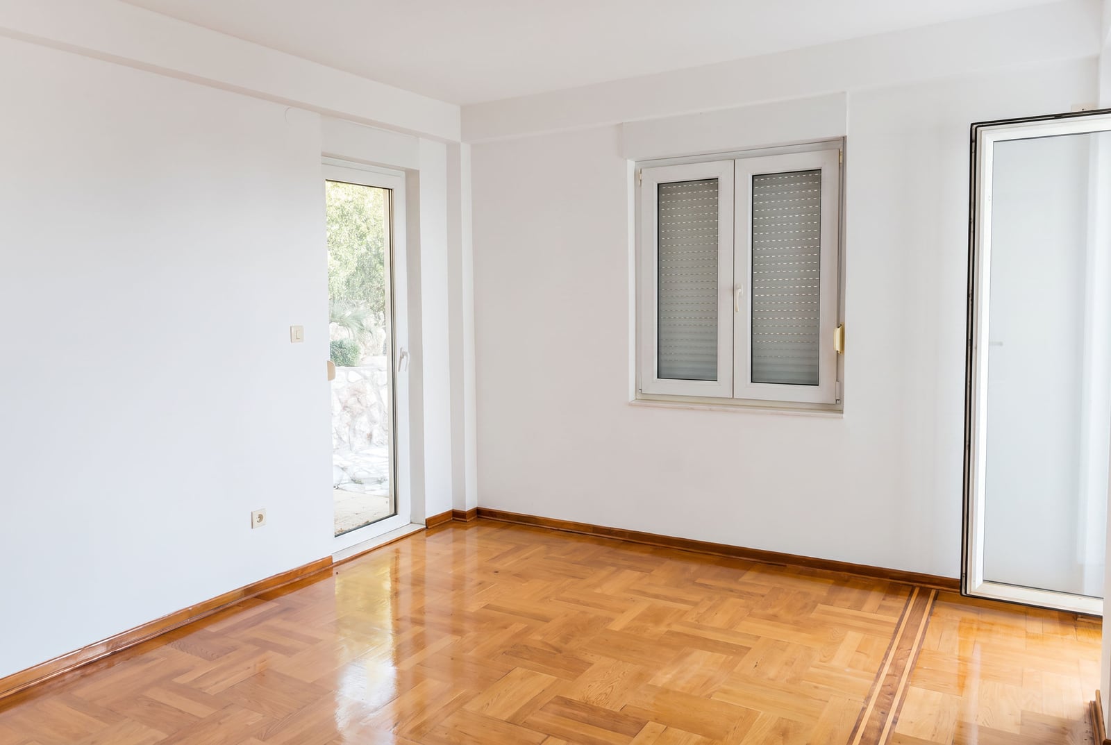 Bright empty living room with parquet flooring, white walls, and balcony access in an apartment in Petrovac, Montenegro.