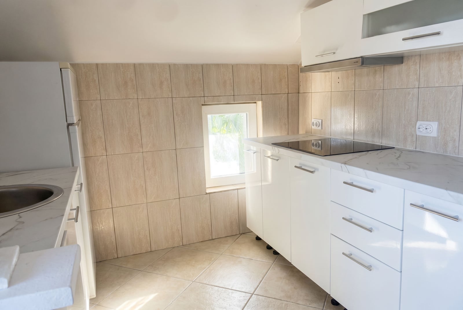 Cuisine blanche moderne dans une maison à Krašići, Monténégro : carrelage clair, appareils électroménagers encastrés et plan de travail en marbre.