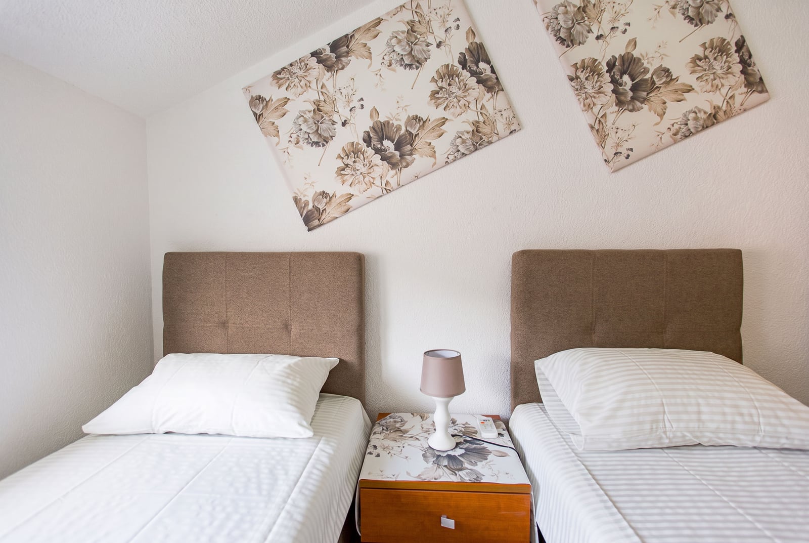 Two single beds with upholstered headboards and a nightstand in the bedroom of an apartment in Budva, Montenegro.
