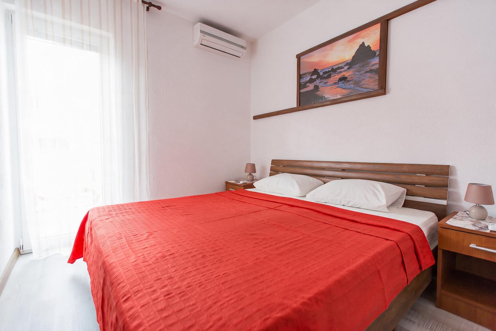 Bedroom with a wooden bed, red bedspread, and nightstands in an apartment in Budva, Montenegro