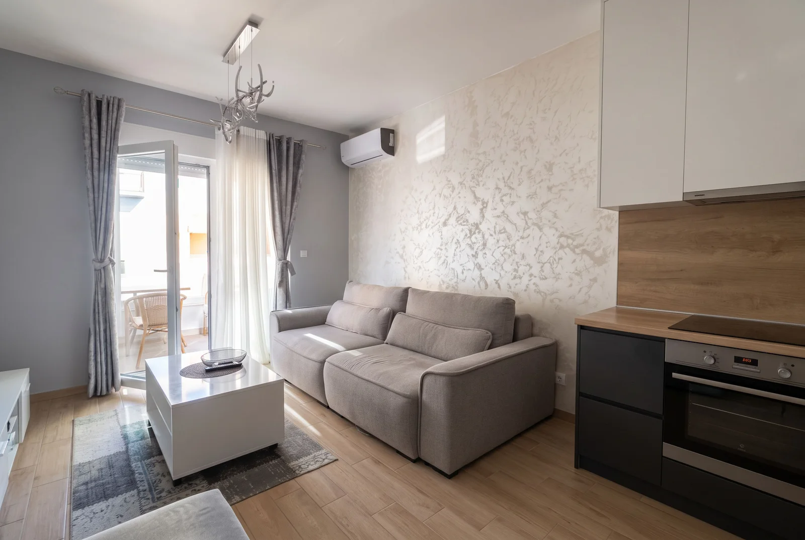 Living room with a grey sofa, white coffee table, and an open kitchen area visible on the right.