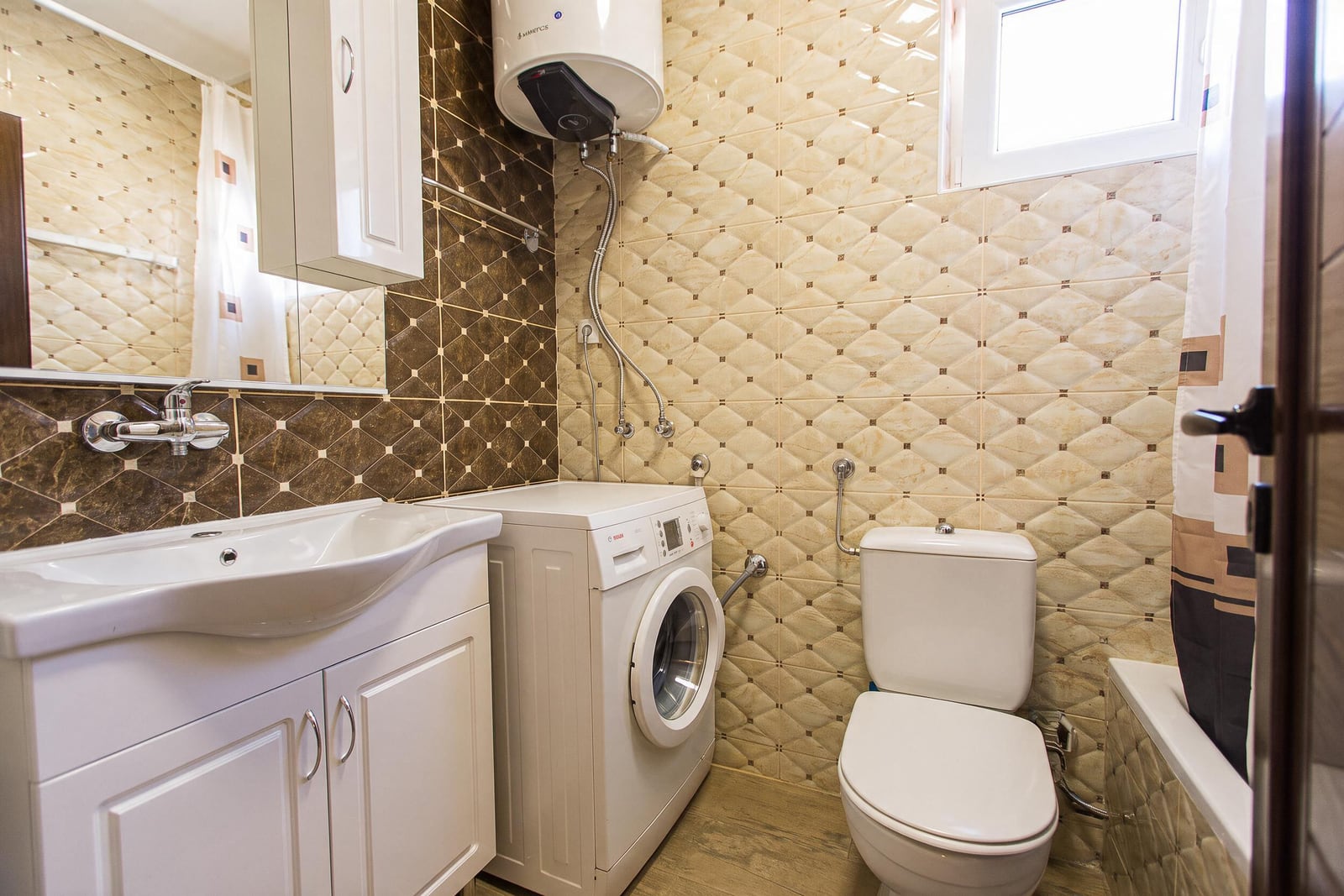 Modern bathroom with white fixtures, washing machine, and water heater in an apartment in Budva, Montenegro.